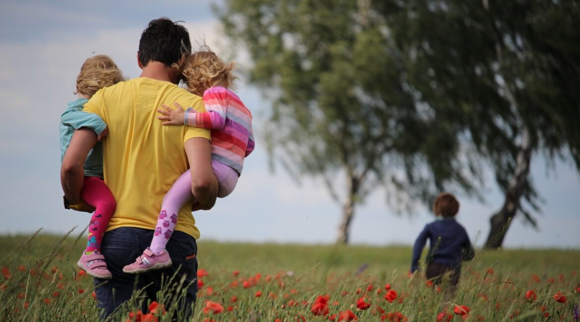 man carrying to girls on field of red petaled flower